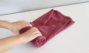 Dłonie zwijają różowy sweter, pokazując, jak składać swetry, by zajmowały mniej miejsca.
