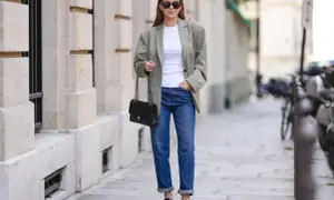 Elegancka kobieta w luźnej marynarce i jeansach, z torebką na łańcuszku. Jej stylizacja to kwintesencja miejskiej elegancji, a brak wzoru w kratę dodaje jej uniwersalności.
