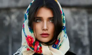 Piękna kobieta z chustą na głowie, ozdobioną kolorowymi kwiatami. Pokazuje, jak wiązać chustę na głowie, tworząc stylowy look.