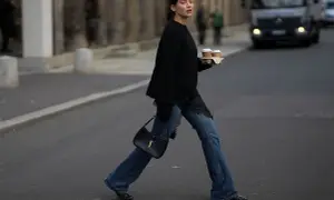 Kobieta w jeansach bootcut i czarnym swetrze z koronkowymi wstawkami niesie kawę. Stylowe jeansy bootcut to podstawa wielu casualowych stylizacji.