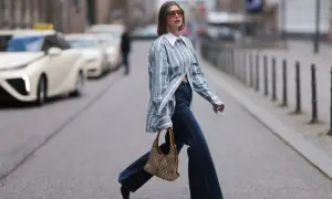 Kobieta w luźnej, pasiastym koszuli i dżinsach pokazuje, jak nosić koszule w miejskim stylu. Torba na ramię dodaje elegancji.