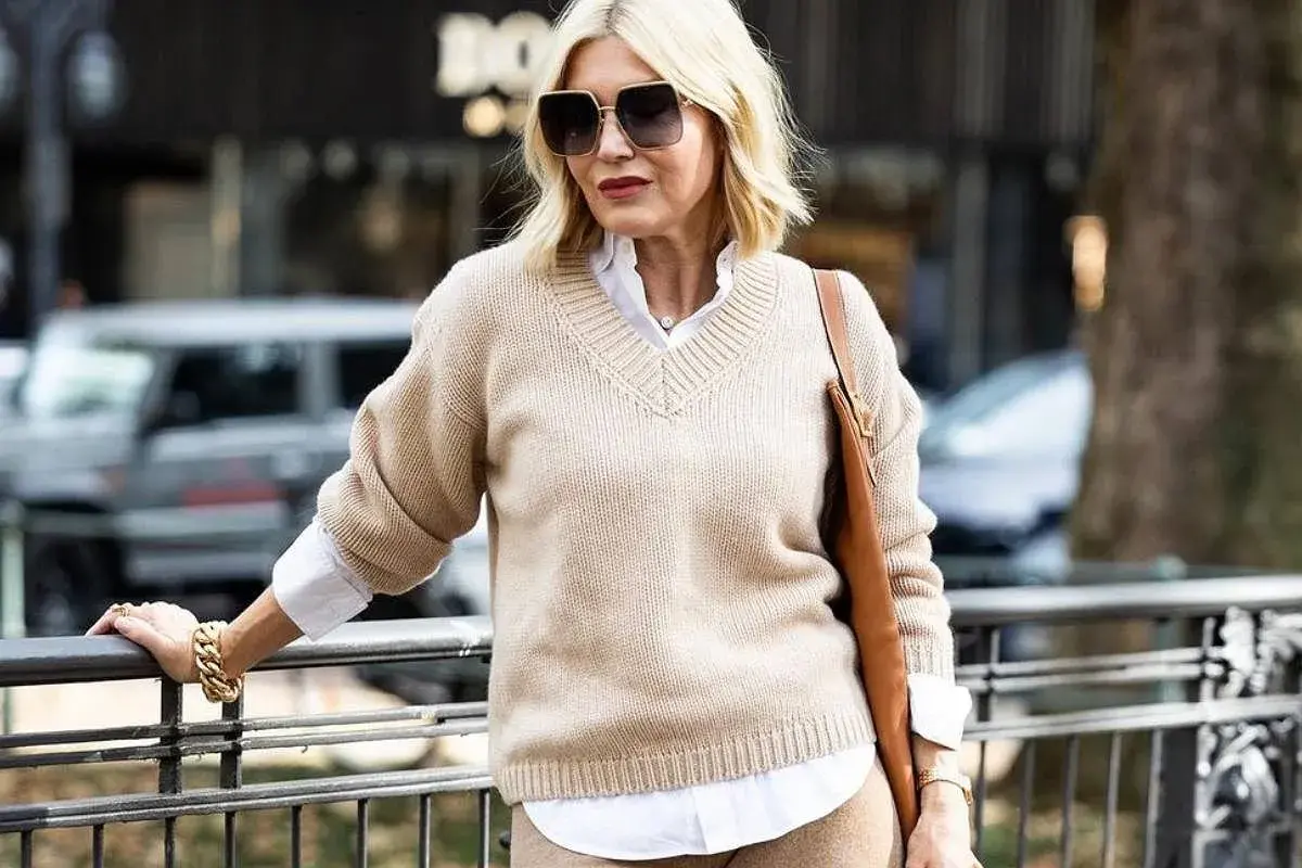 Eleganckie zestawy ubrań dla 50-latki: beżowy sweter, biała koszula i brązowa torebka. Stylowa kobieta w modnej stylizacji.
