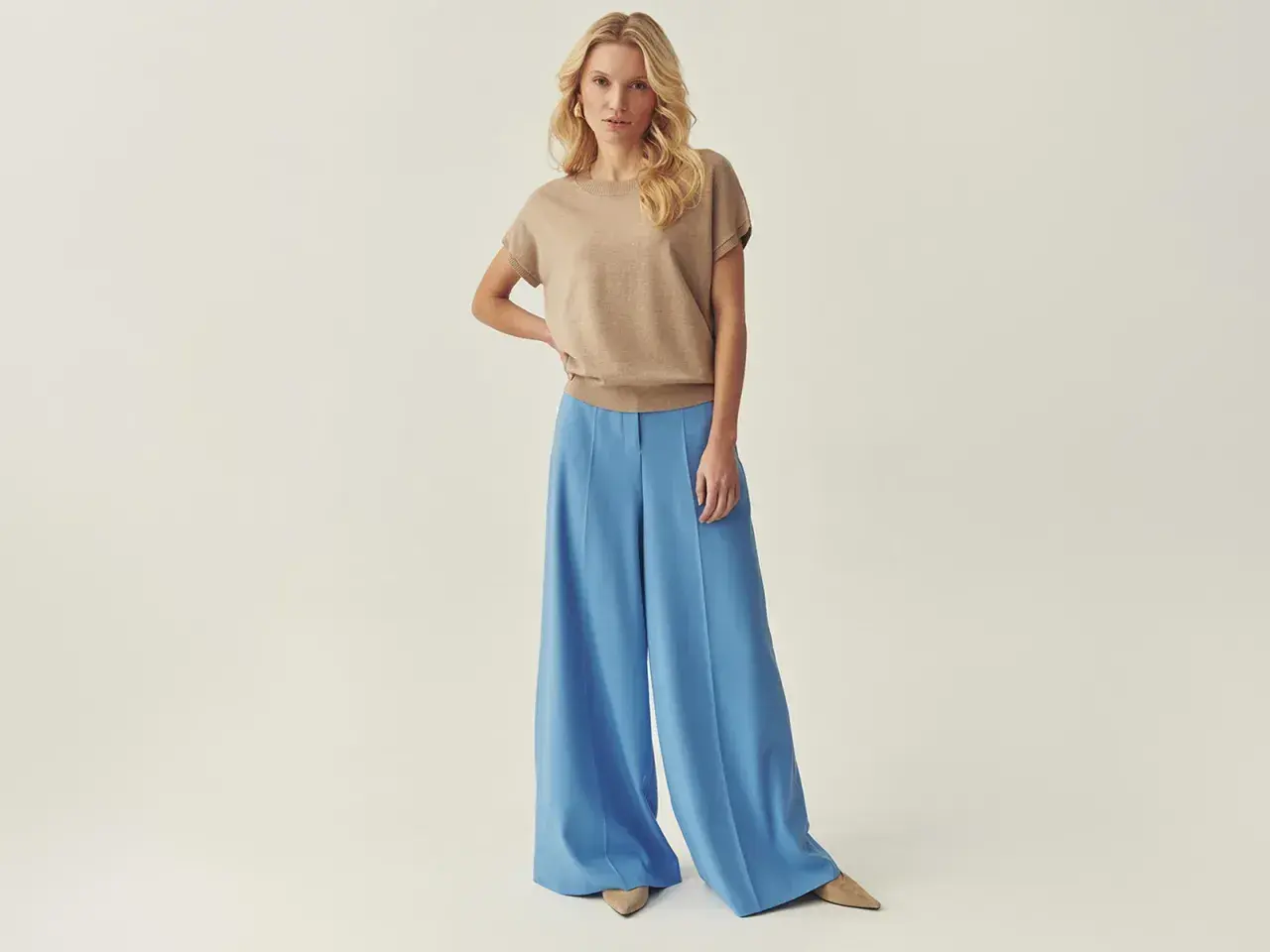 Modelka prezentuje stylizację: jaka bluzka do szerokich spodni? Beżowy sweterek i błękitne, lejące się spodnie palazzo.