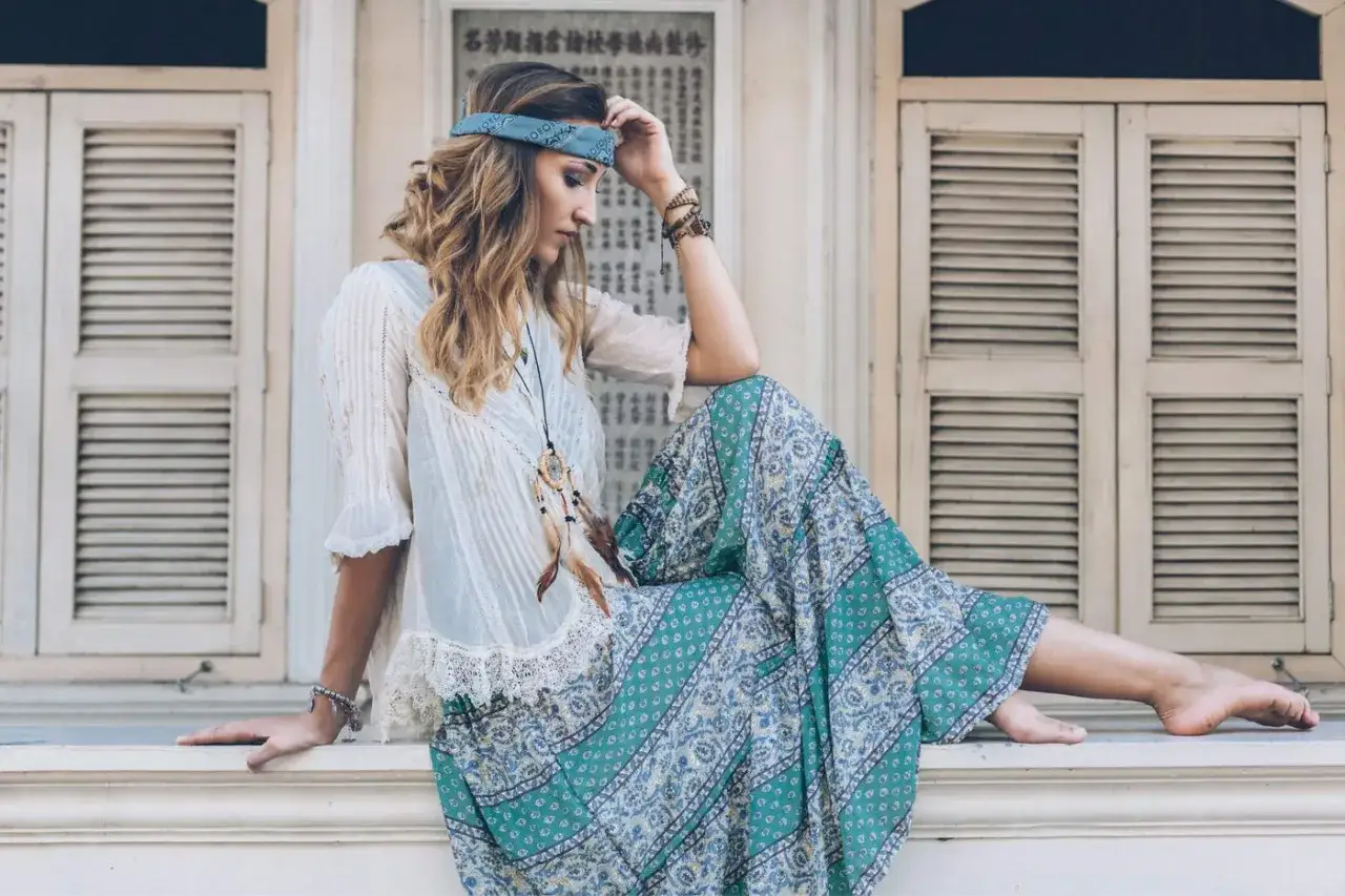 Kobieta w stylizacji boho, z opaską na głowie i długą, wzorzystą spódnicą, siedzi na parapecie.