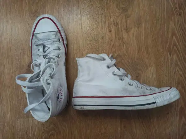 Białe trampki na drewnianym tle. Pokazują, jak wiązać trampki, z luźno zwisającymi sznurówkami.