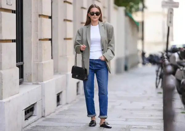 Elegancka kobieta w luźnej marynarce i jeansach, z torebką na łańcuszku. Jej stylizacja to kwintesencja miejskiej elegancji, a brak wzoru w kratę dodaje jej uniwersalności.